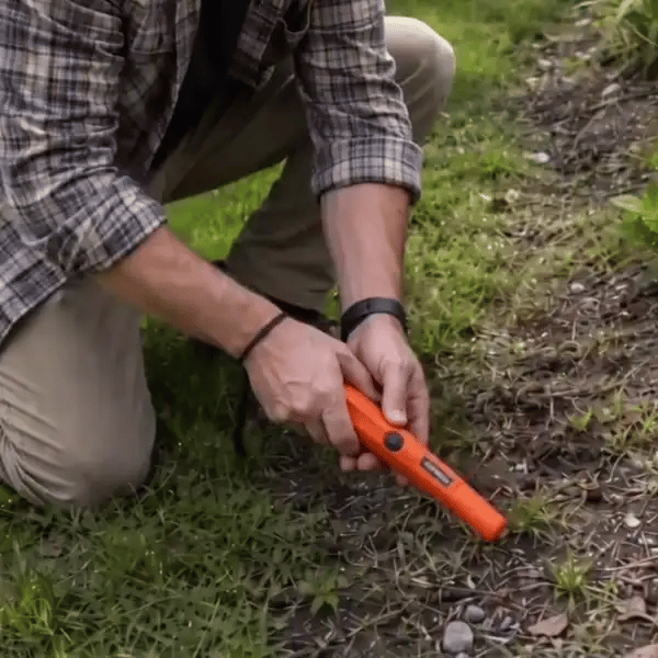 Una mano con el detector sobre la arena y una cadena asomando