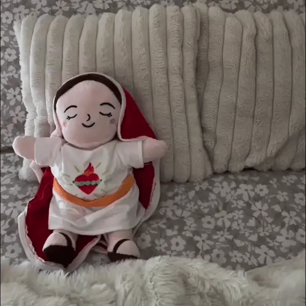 Niña dormida abrazando el peluche de la Virgen encendido